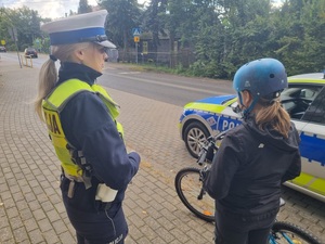 Mała rowerzystka w kasku otrzymanym od policjantów z umundurowaną policjantką, stojące przy oznakowanym radiowozie.