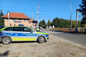 Policjant stoi przy przejeździe kolejowym, obok radiowóz.