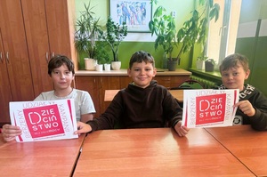 Trzech chłopców siedzi w ławce. Trzymają w rekach plakaty kampanii z napisem "Dzieciństwo bez przemocy".